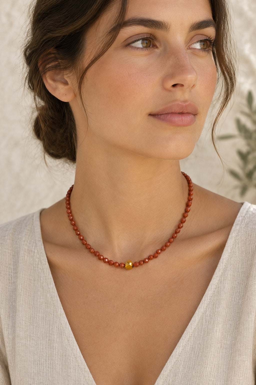 A beaded necklace made of small faceted orange-brown beads with a single central gold bead, displayed against a plain light gray background.